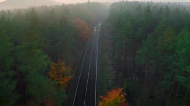 有亮前灯的汽车在多云的夜晚行驶在高速公路上穿过秋天的森林.荒野中的沥青双车道公路，被雾气笼罩着